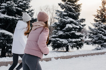 Two young athletic girls running in the park on a sunny winter day. A healthy way of life.