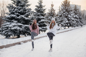Two young athletic girls do a warm-up before running on a sunny winter day. A healthy way of life.