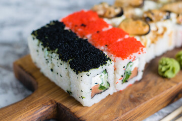 Delicious sushi rolls with red fish, caviar, mussels, cheese, red ginger, wasabi and soy sauce on a wooden board on a light background with copy space
