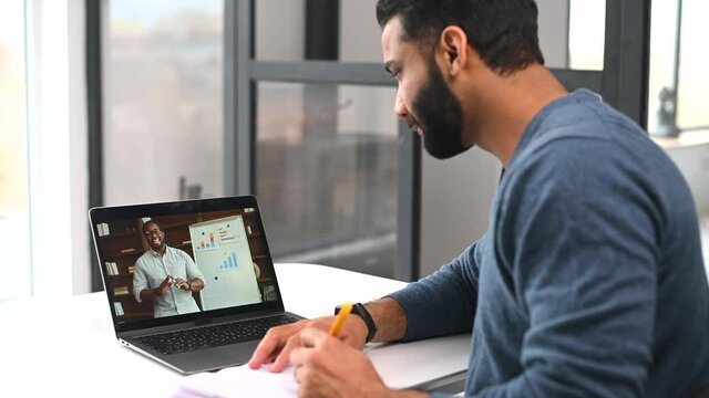 E-learning. Multiracial Indian man using laptop computer for watching online courses, webinars, takes notes, African male tutor on the screen, latin guy taking language classes