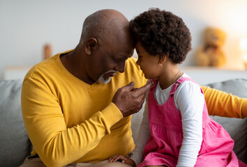 Happy elderly african american man and little girl touches foreheads and enjoying time together at home