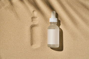 a bottle of serum with a pipette on a beige sand background 