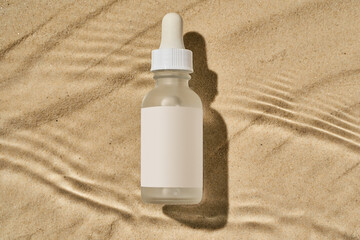 a bottle of serum with a pipette on a beige sand background in the water