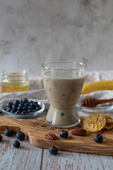 Glass of vegan cocktail or smoothy made from oat milk with bananas, blueberries and honey on an olive wooden board.