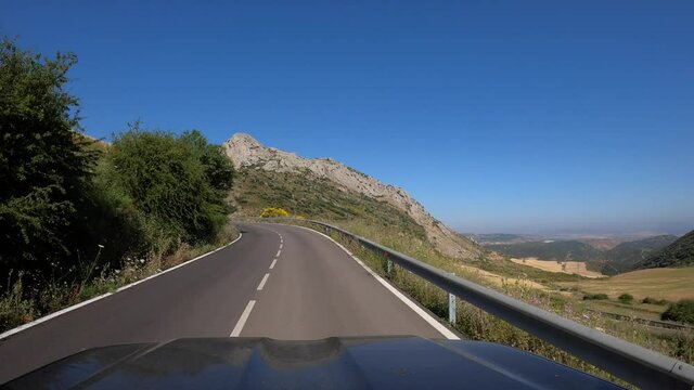 POV of car driving on straight two way old asphalt road through a mountain in the provinces of Malaga, southern Spain. To drive through a spanish rural area with mountains at Andalusia. -Dan
