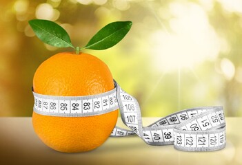 Fruit orange is wrapped with measuring tap as a symbol of cellulite on the skin. - obrazy, fototapety, plakaty