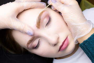 close-up alignment of the contour of the eyebrows with a cotton swab after the procedure lamination and coloring of the eyebrows