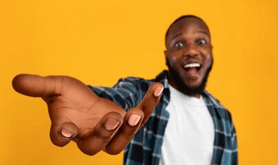 Happy african american guy outstretching hand, holding something invisible
