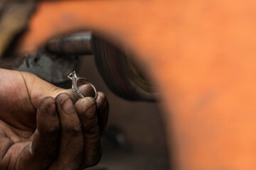 Artisan holding a ring with diamonds next to a machine in a workshop