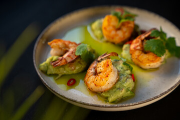 Appetizer with shrimps served with guacamole and greens on white plate on black background. Delicious, beautiful, healthy snack. Modern cuisine