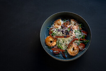 Appetizer with shrimps. Salad with greens, vegetables and cheese on black background. Delicious, beautiful, healthy snack. Modern cuisine. Top view