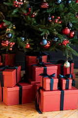 Christmas gifts under a snowy tree, beautiful red boxes. Gift for the new year. Beautiful box with a bow. Dark background.