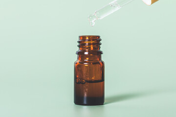 Essential oil drop drips from pipette into brown glass bottle