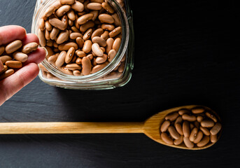Overhead image of a hand, a glass jar and a wooden spoon with beans on black background. 