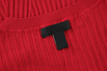 Close-up of a black label on a red sweater. Label on the back of the neckline of the sweater. Blank...