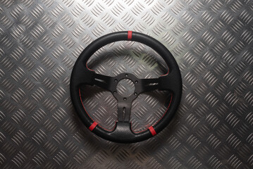 Black sport steering wheel on the metal flat lay background.
