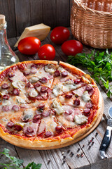 Homemade pizza with sausage, pickles, tomato and cheese on a table. Tasty food