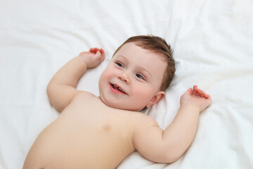 A boy in diapers on a bed in a snow-white bedroom