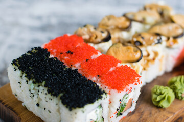 Delicious sushi rolls with red fish, caviar, mussels, cheese, red ginger, wasabi and soy sauce on a wooden board on a light background with copy space