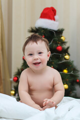 Obraz na płótnie Canvas Happy kid in diapers on the bed in the bedroom with a christmas tree