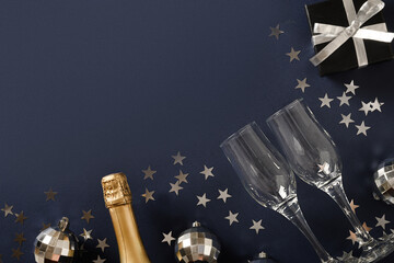 Composition with New Year champagne, drinking straws, shiny silver disco balls on blue navy background. View from above. Festive greeting card or invitation for party with copy space.
