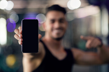 Sports App. Happy young arab man holding and pointing at blank smartphone