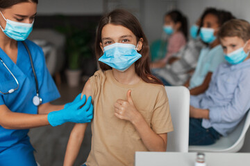 Vaccinated Girl Wearing Face Mask And Gesturing Thumbs Up Indoors