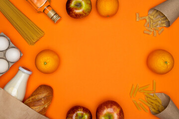 Bread and bottle of milk in paper eco bag. Spaghetti, sunflower oil, eggs and red apple on orange...