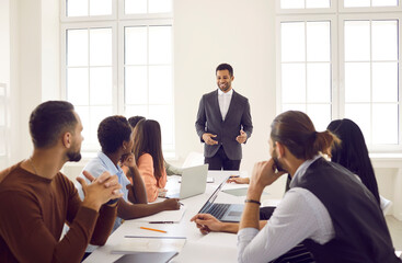 Young ambitious male employee speaks to colleagues at business meeting at desk in office. Businessman, mentor coach or business speaker with colleagues makes plan to increase business efficiency.