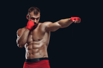 Front view of a sporty man in boxing gloves practicing fighting techniques isolated on black background