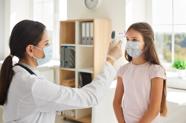Nurse or doctor using modern digital infrared thermometer and pointing it at kid's forehead. Child who's wearing face mask gets body temperature checked at hospital. Covid 19, health, safety concepts