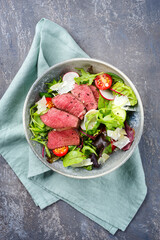 Modern style traditional fried dry aged bison beef rump steak slices with vegetable, lettuce and parmesan cheese served as top view in a Nordic design bowl with copy space