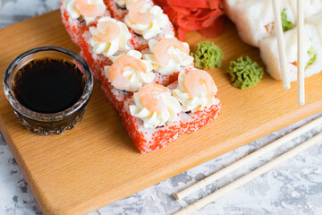 Delicious sushi rolls with chicken, cheese, shrimp, red ginger, wasabi and soy sauce on a wooden board on a light background with copy space