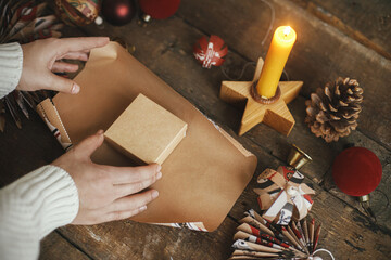 Wrapping christmas gift. Hands wrapping gift box in festive craft red paper on rustic wooden table...