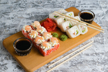 Delicious sushi rolls with chicken, cheese, shrimp, red ginger, wasabi and soy sauce on a wooden board on a light background with copy space