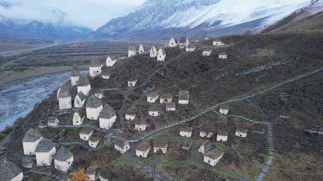 Flying around Ethnic Tombs Dargavs in North Ossetia. In the background there is a mountain river and the snow-capped Caucasus mountains.