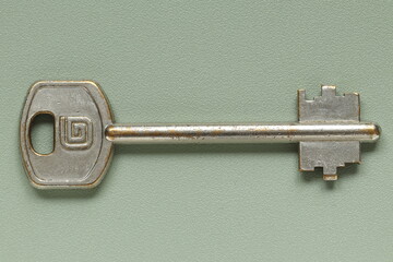 Old key from the door lock on a green background. Old key. 