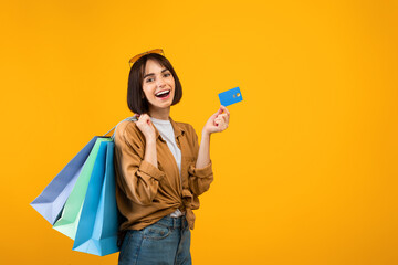 Cashback concept. Happy woman holding credit card and bright shopping bags, posing over yellow...