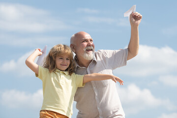 Grandfather and son playing with toy paper plane against summer sky background. Child boy with dreams of flying. Family Relationship Grandfather and child.