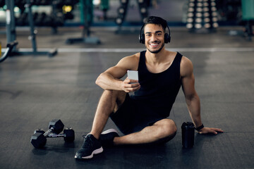 Fototapeta na wymiar Handsome Arab Athlete Relaxing With Smartphone After Training In Gym