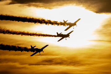 Lot formacji trzech samolotów akrobacyjnych ze smugaczem na tle słońca - obrazy, fototapety, plakaty