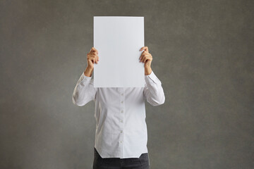 Business man holding up a banner against a white background instead of his head. Cardboard placard is blank ready for your message. In a white shirt on a gray background
