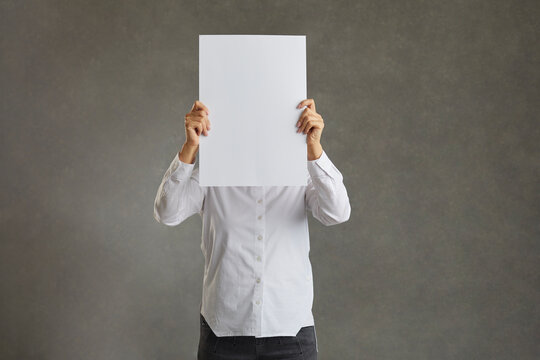 Business Man Holding Up A Banner Against A White Background Instead Of His Head. Cardboard Placard Is Blank Ready For Your Message. In A White Shirt On A Gray Background