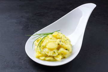 Traditional German potato salad with onion and chives served as close-up in a design bowl on a rustic black board with copy space