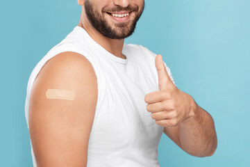 Smiling adult caucasian man with band aid on hand after injection show thumb up isolated on blue...