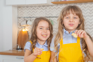 Happy preschool girls taste the cookies just cooked together in the kitchen.