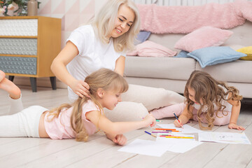 30 years old caucasian mother helping her cute litte daughters draw together