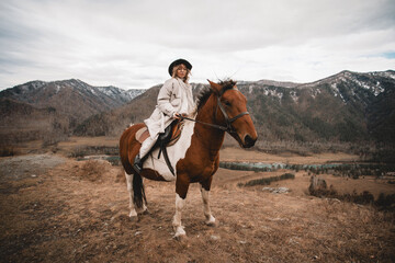 Fototapeta na wymiar Beautiful young female horse owner taking care of her horse with mountain on background. Animal and people frienship concept. Autumn in Altai