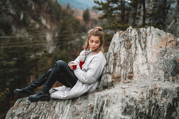 Travel girl drinking hot tea from thermos on forest and mountain background. Girl on vacation enjoying the beauty of nature. Camping hiking lifestyle. Altai mountains