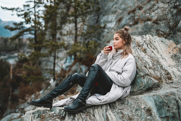 Travel girl drinking hot tea from thermos on forest and mountain background. Girl on vacation enjoying the beauty of nature. Camping hiking lifestyle. Altai mountains